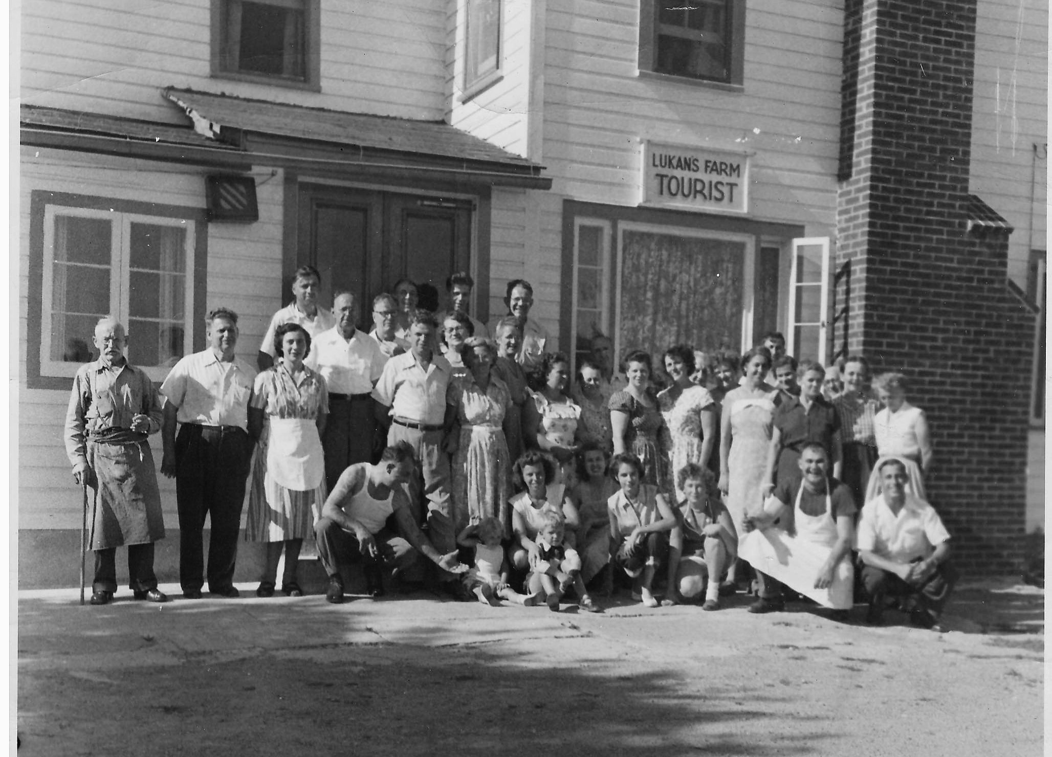 Group photo outside Lukans Farm Tourist, featuring diverse individuals, some in traditional attire. A sense of community and hospitality is evident.