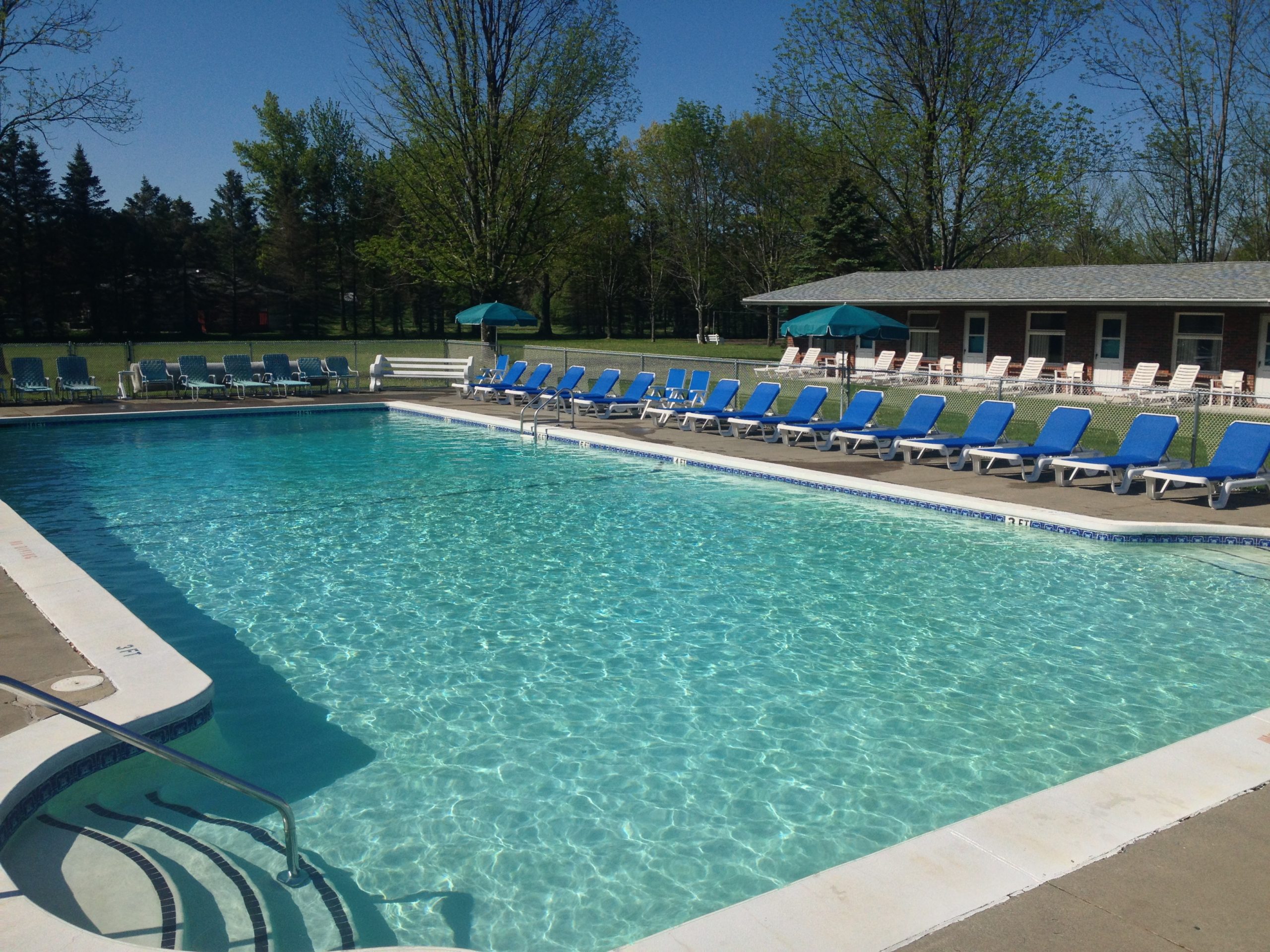 Inviting swimming pool surrounded by blue lounge chairs and green trees, ideal for relaxation and leisure activities. Perfect for summer enjoyment.